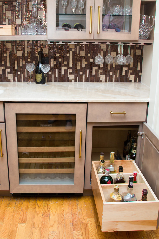 Photo of a small contemporary single-wall wet bar in Houston with an undermount sink, shaker cabinets, beige cabinets, marble benchtops, brown splashback, glass tile splashback, light hardwood floors and brown floor.