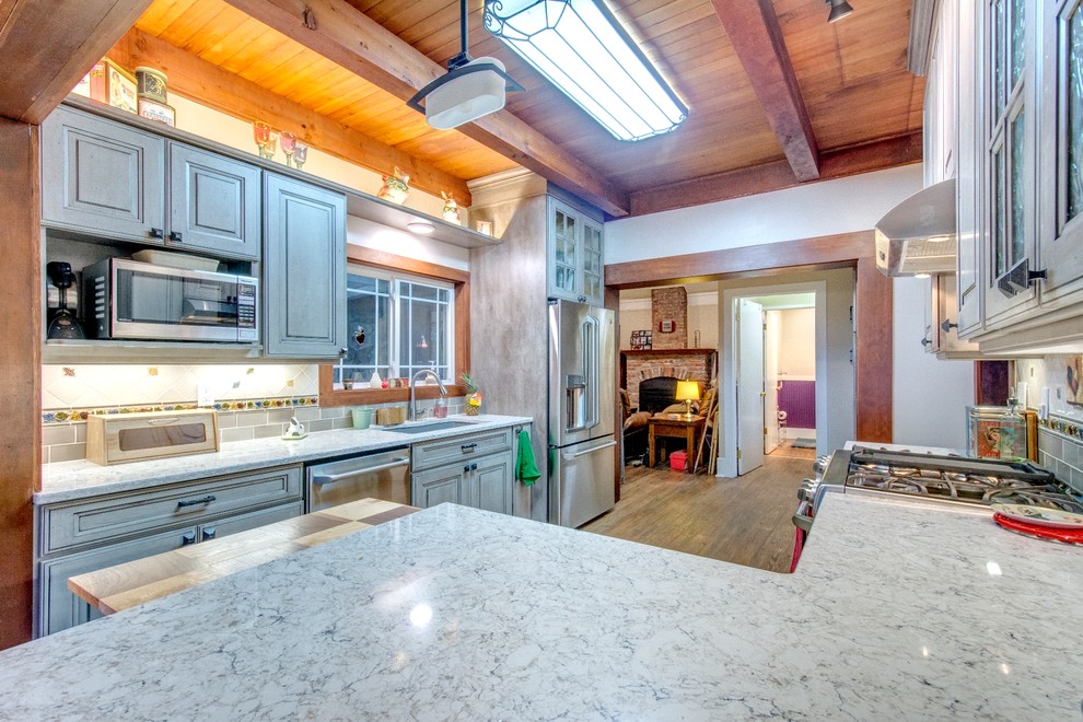 Kitchen - mid-sized rustic medium tone wood floor kitchen idea in Portland with an undermount sink, raised-panel cabinets, gray cabinets, quartz countertops, ceramic backsplash and stainless steel appliances