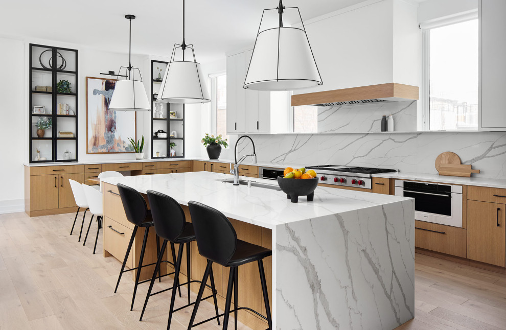 This is an example of a contemporary open plan kitchen in Chicago with flat-panel cabinets, light wood cabinets, engineered stone countertops, white splashback, engineered quartz splashback, light hardwood flooring, an island and white worktops.