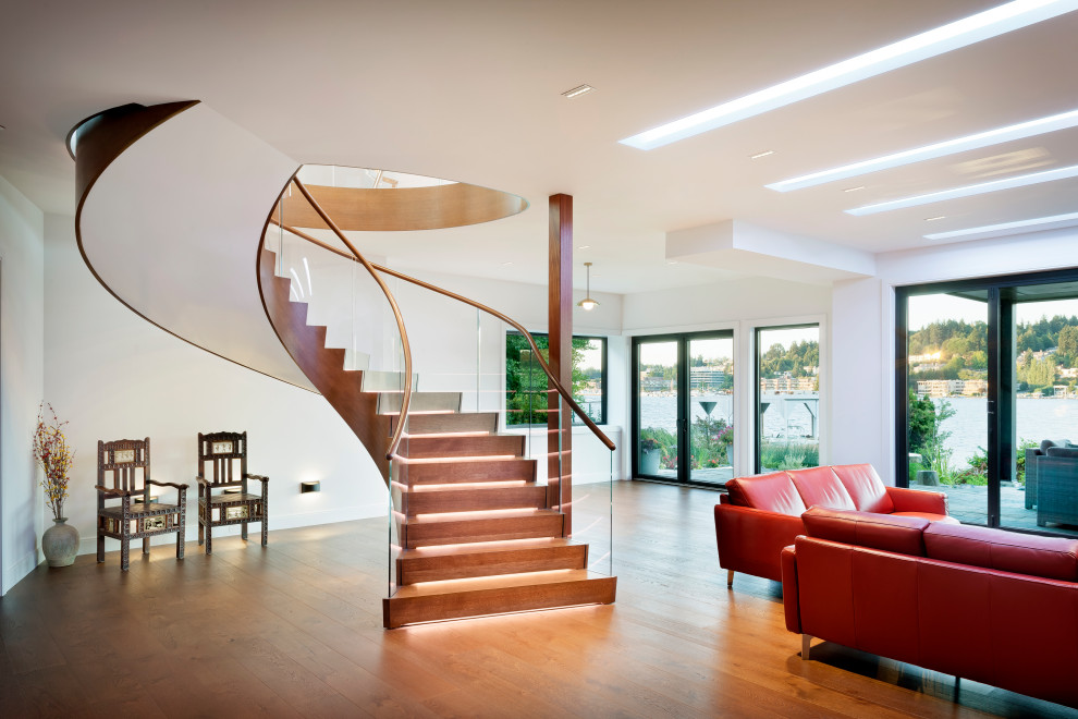 На фото: изогнутая лестница в современном стиле с деревянными ступенями и стеклянными перилами без подступенок с