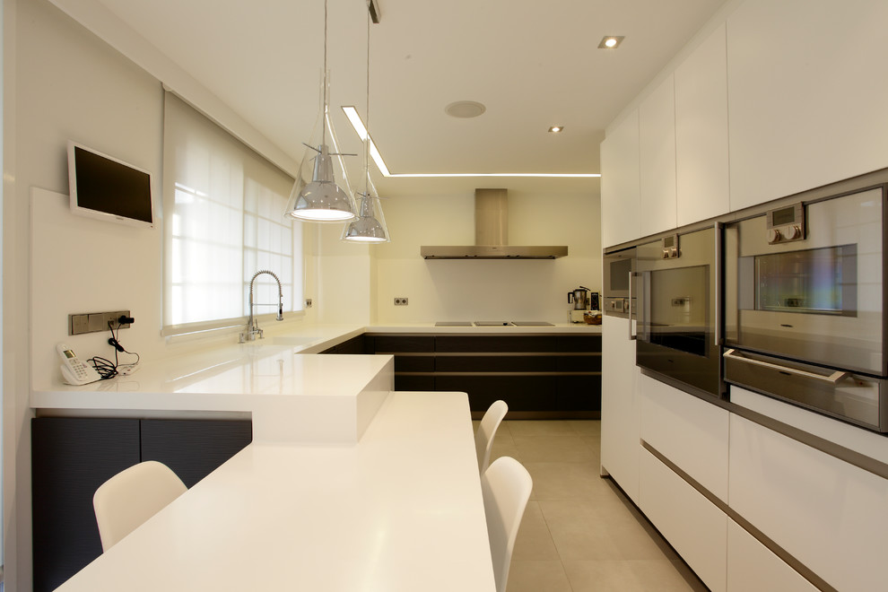 Mid-sized modern l-shaped eat-in kitchen in Madrid with a drop-in sink, flat-panel cabinets, white cabinets, white splashback, stainless steel appliances, ceramic floors, a peninsula, grey floor and white benchtop.