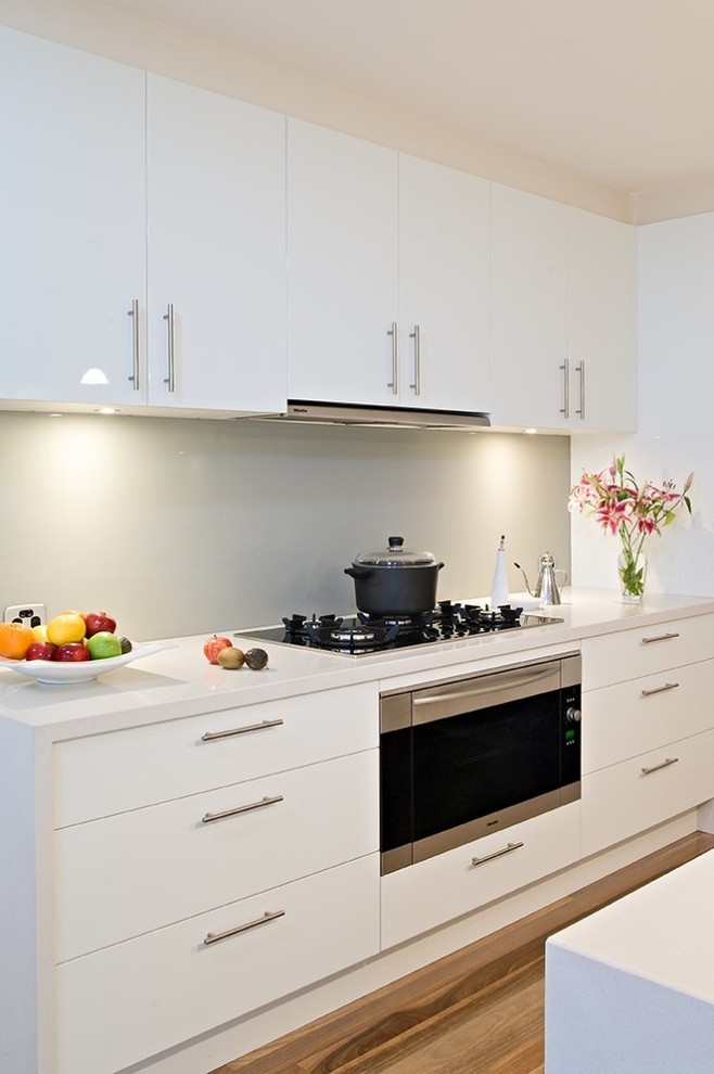 Design ideas for a large modern l-shaped open plan kitchen in Melbourne with an undermount sink, flat-panel cabinets, white cabinets, quartz benchtops, grey splashback, glass sheet splashback, stainless steel appliances, medium hardwood floors and with island.