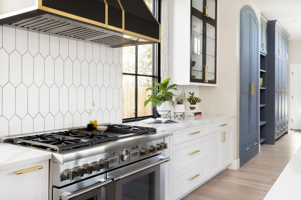 Mid-sized eclectic l-shaped light wood floor kitchen pantry photo in Denver with a single-bowl sink, shaker cabinets, white cabinets, quartz countertops, white backsplash, ceramic backsplash, stainless steel appliances, an island and white countertops