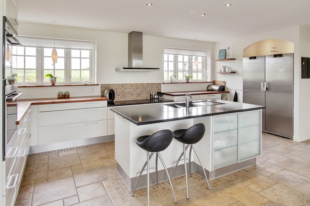 Design ideas for a large transitional l-shaped eat-in kitchen in Odense with a double-bowl sink, shaker cabinets, white cabinets, wood benchtops, beige splashback, mosaic tile splashback, stainless steel appliances, with island and ceramic floors.