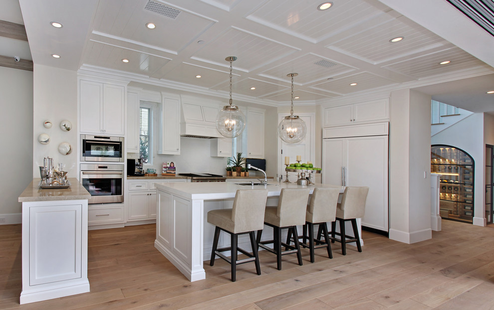 This is an example of a beach style u-shaped kitchen in Orange County with shaker cabinets, white cabinets, white splashback, panelled appliances, medium hardwood floors and with island.