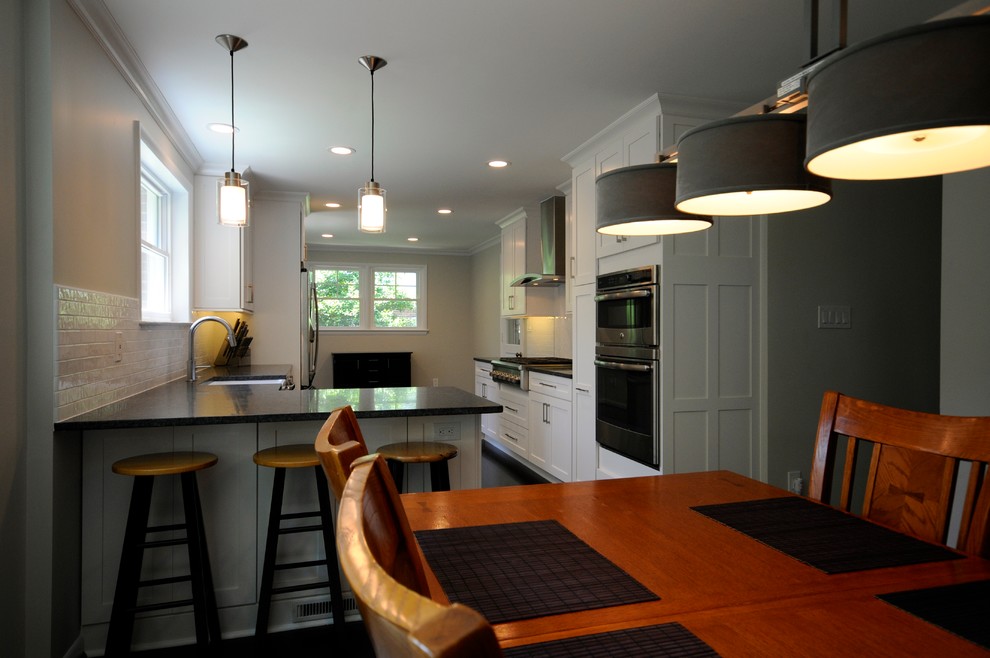 Mid-sized transitional galley eat-in kitchen in DC Metro with a farmhouse sink, shaker cabinets, white cabinets, granite benchtops, white splashback, subway tile splashback, stainless steel appliances, dark hardwood floors and a peninsula.