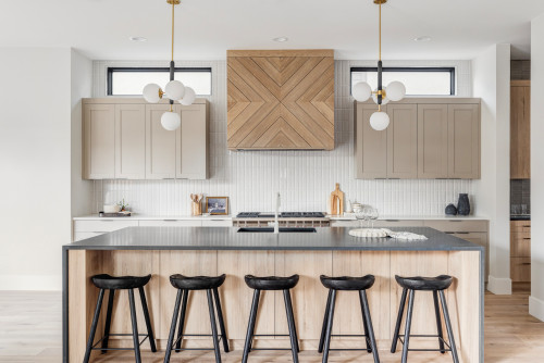 Modern island kitchen with shaker wall cabinets, herringbone wood range hood, globe pendants, and a black countertop island with five stools