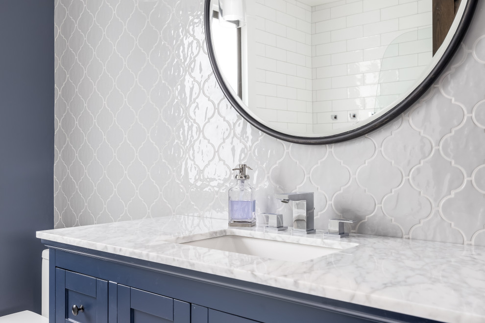 Alcove bathtub - mid-sized transitional white tile ceramic tile, white floor, single-sink and wainscoting alcove bathtub idea in Minneapolis with shaker cabinets, blue cabinets, a one-piece toilet, blue walls, an undermount sink, marble countertops, a hinged shower door and a freestanding vanity