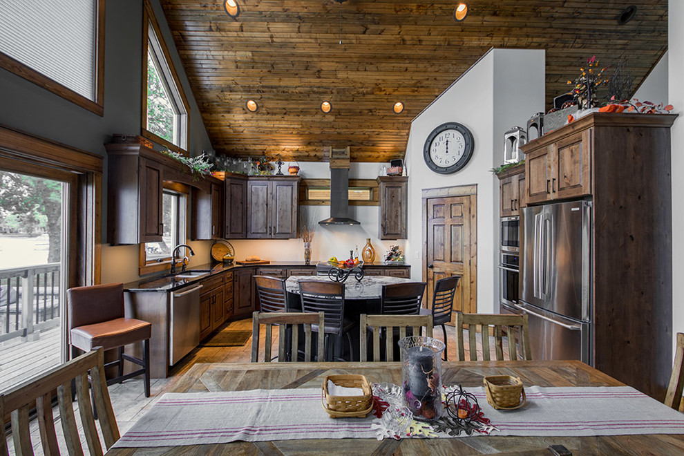 Example of a mountain style porcelain tile kitchen design with an undermount sink, raised-panel cabinets, distressed cabinets, granite countertops and stainless steel appliances