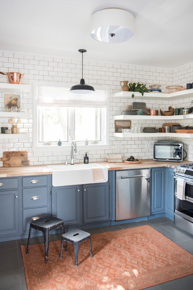 Photo of a beach style l-shaped kitchen in Seattle with a farmhouse sink, raised-panel cabinets, blue cabinets, wood benchtops, white splashback, subway tile splashback, stainless steel appliances, no island and grey floor.