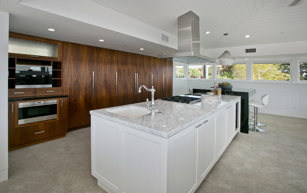 This is an example of a large contemporary u-shaped open plan kitchen in Los Angeles with a farmhouse sink, flat-panel cabinets, medium wood cabinets, quartzite benchtops, stainless steel appliances, limestone floors and multiple islands.