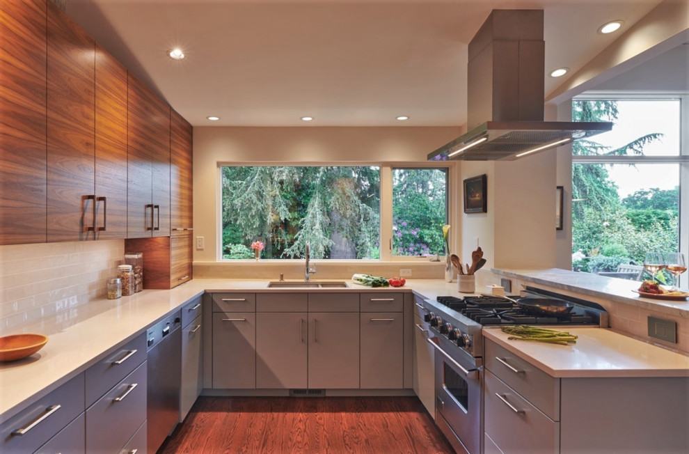 Design ideas for a mid-sized midcentury u-shaped eat-in kitchen in Seattle with an undermount sink, flat-panel cabinets, medium wood cabinets, solid surface benchtops, white splashback, ceramic splashback, stainless steel appliances, dark hardwood floors, a peninsula, brown floor, white benchtop and vaulted.