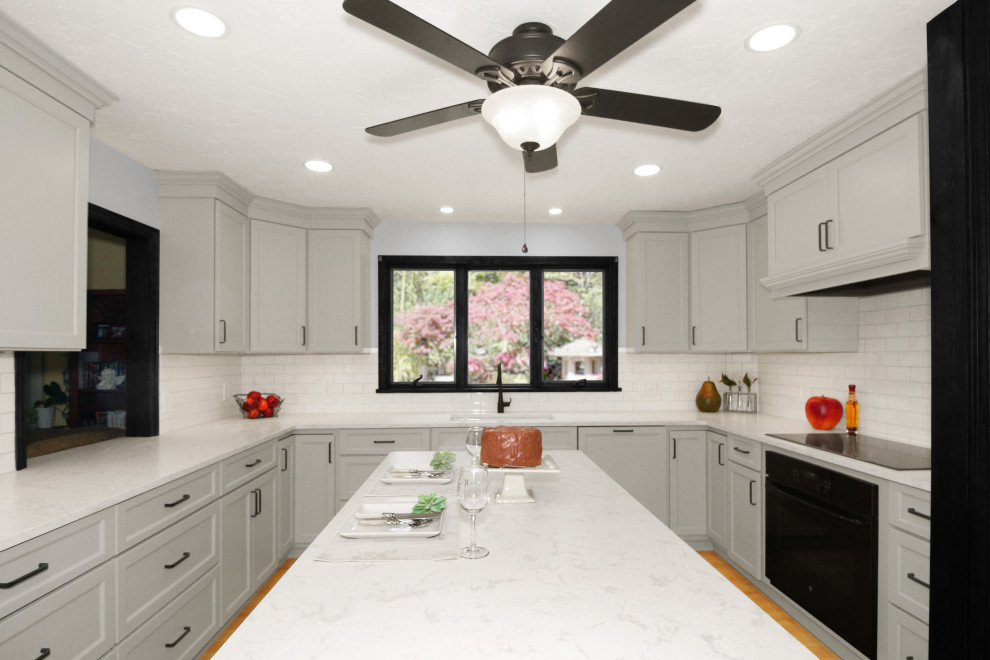 Large transitional u-shaped light wood floor and brown floor enclosed kitchen photo in Boston with a double-bowl sink, shaker cabinets, gray cabinets, quartz countertops, white backsplash, porcelain backsplash, black appliances, an island and white countertops