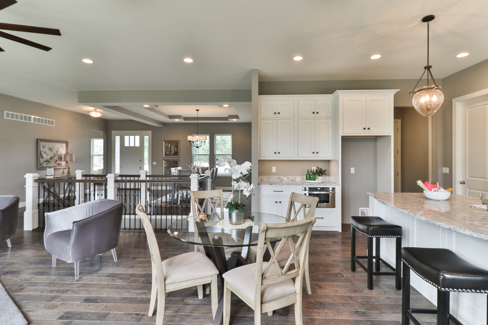 Mid-sized transitional l-shaped dark wood floor and brown floor open concept kitchen photo in St Louis with a farmhouse sink, shaker cabinets, white cabinets, granite countertops, gray backsplash, stainless steel appliances and an island