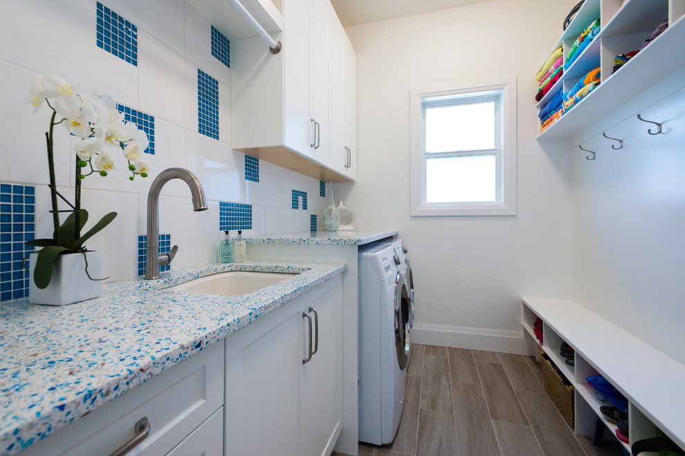 Inspiration for a mid-sized transitional galley utility room in Vancouver with an undermount sink, shaker cabinets, white cabinets, recycled glass benchtops, grey walls, porcelain floors and a side-by-side washer and dryer.