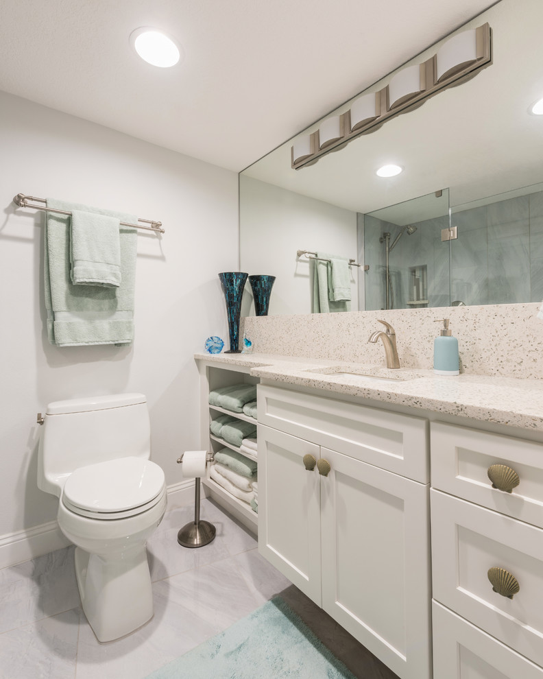 Photo of a large transitional 3/4 bathroom in Orlando with shaker cabinets, white cabinets, a corner shower, gray tile, porcelain tile, grey walls, porcelain floors, an undermount sink, recycled glass benchtops, grey floor, a hinged shower door and white benchtops.