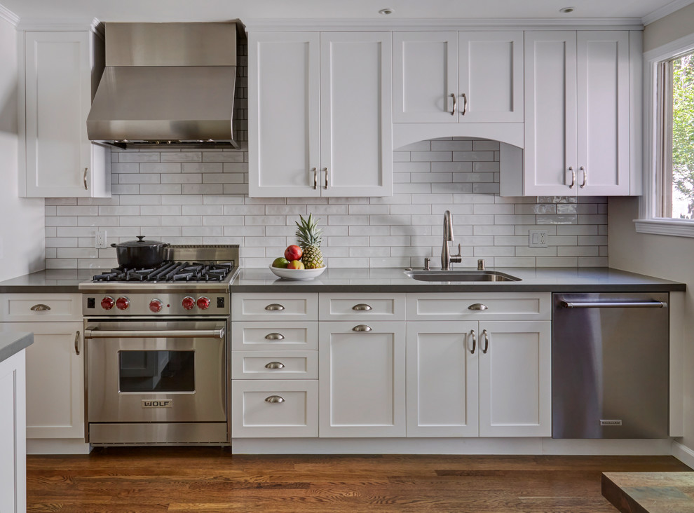 This is an example of a mid-sized transitional u-shaped separate kitchen in San Francisco with a single-bowl sink, shaker cabinets, white cabinets, quartz benchtops, white splashback, subway tile splashback, stainless steel appliances, medium hardwood floors, no island, brown floor and grey benchtop.