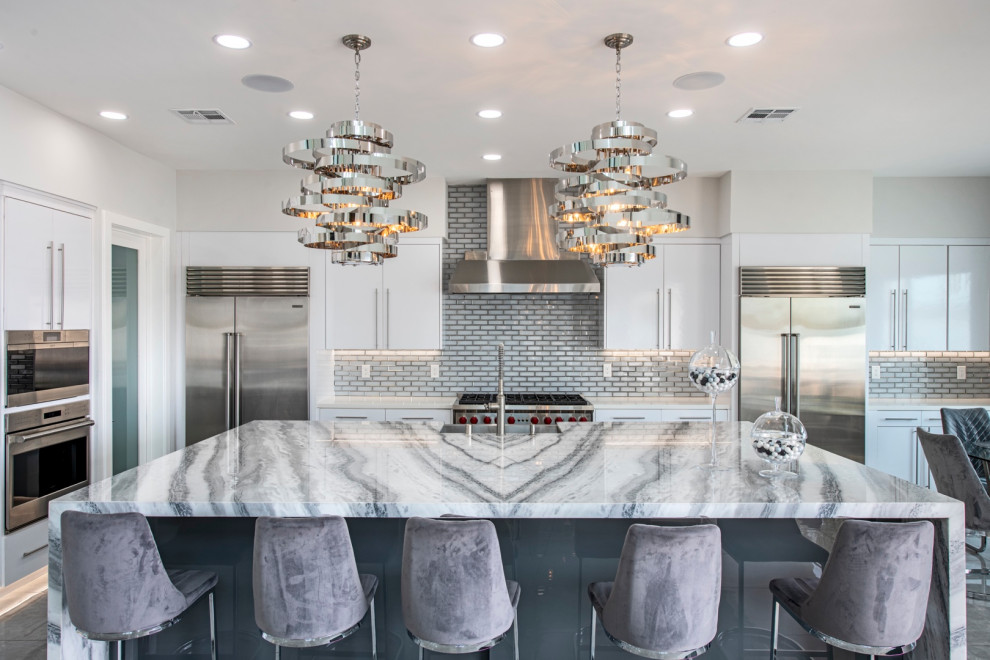 This is an example of an expansive contemporary galley open plan kitchen in Las Vegas with an undermount sink, flat-panel cabinets, white cabinets, granite benchtops, glass tile splashback, stainless steel appliances, ceramic floors, with island, grey floor and white benchtop.