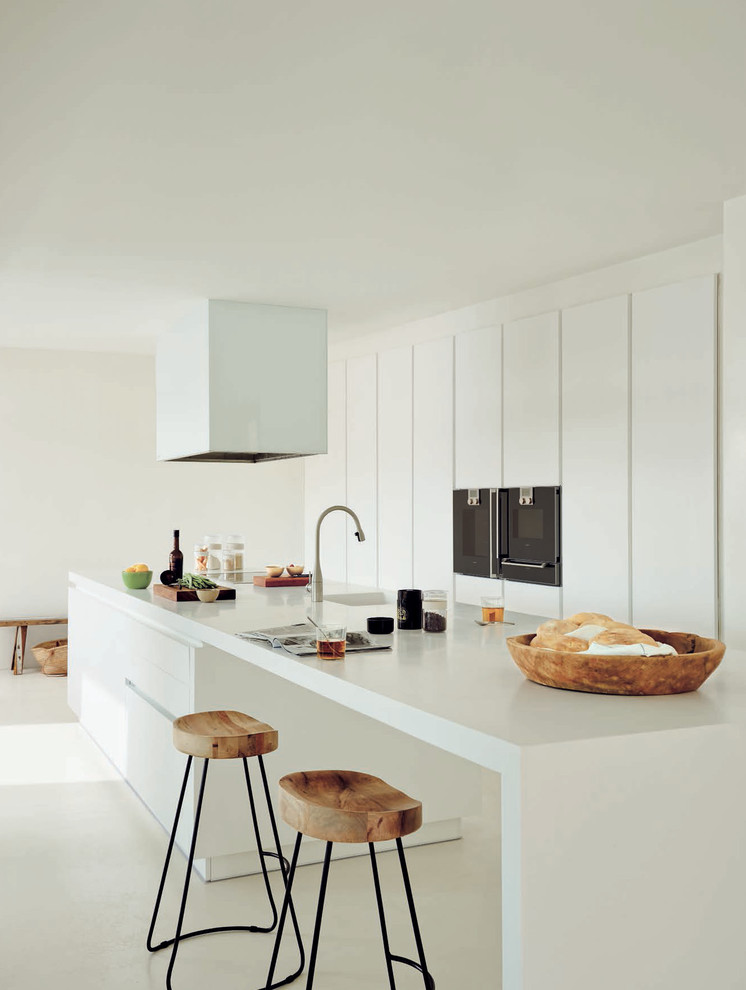 Large contemporary galley kitchen in Madrid with an integrated sink, flat-panel cabinets, white cabinets, solid surface benchtops, with island, black appliances and white benchtop.