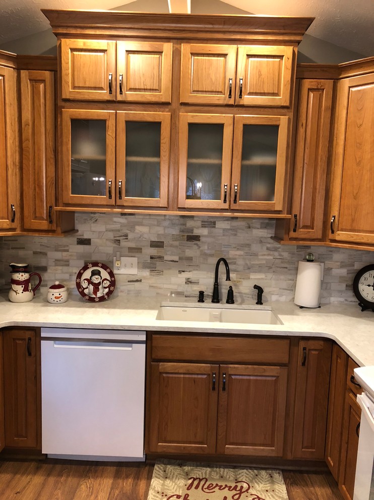 Inspiration for a mid-sized transitional u-shaped laminate floor and brown floor eat-in kitchen remodel in Omaha with an undermount sink, raised-panel cabinets, medium tone wood cabinets, quartz countertops, beige backsplash, stone tile backsplash, white appliances and white countertops