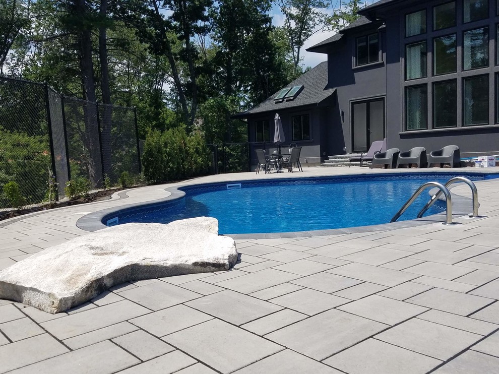 Large backyard custom-shaped natural pool in Boston with concrete pavers.
