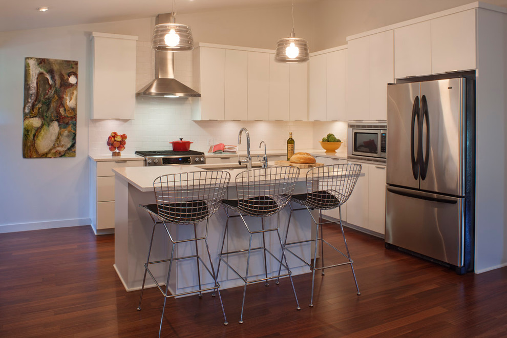 Mid-sized modern l-shaped eat-in kitchen in Austin with stainless steel appliances, subway tile splashback, flat-panel cabinets, white cabinets, quartz benchtops, white splashback, with island, an undermount sink, dark hardwood floors and brown floor.