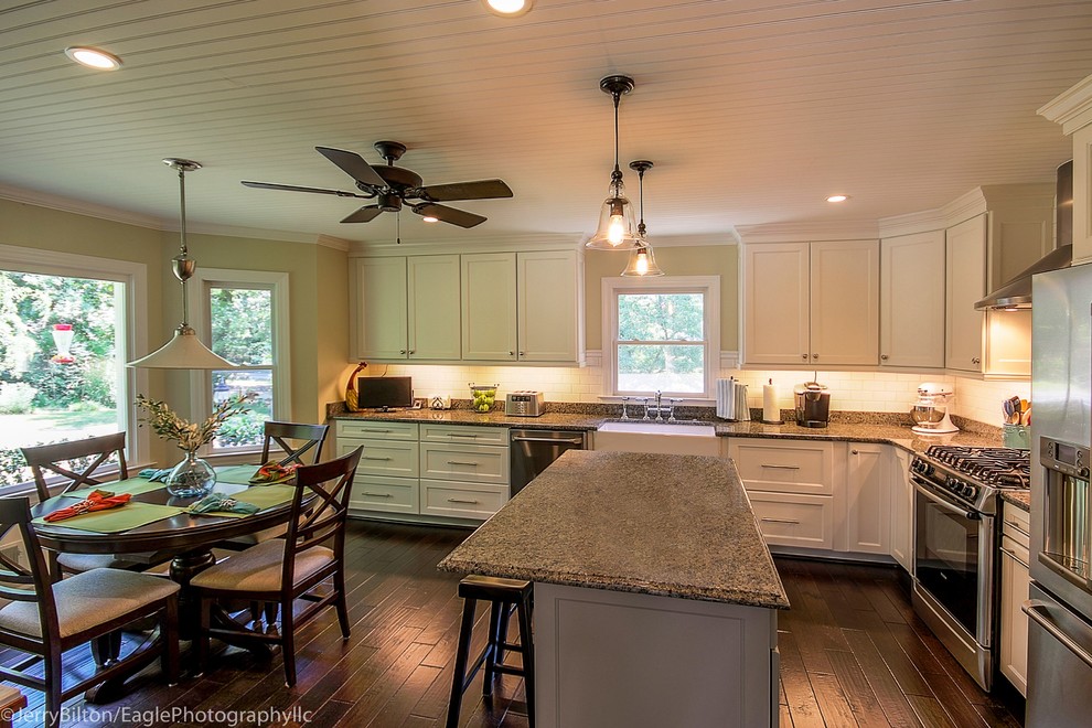 Example of a large transitional l-shaped dark wood floor and brown floor eat-in kitchen design with a farmhouse sink, shaker cabinets, white cabinets, granite countertops, white backsplash, subway tile backsplash, stainless steel appliances and an island