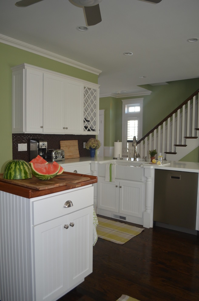 Mid-sized transitional l-shaped dark wood floor eat-in kitchen photo with a farmhouse sink, beaded inset cabinets, white cabinets, solid surface countertops, gray backsplash, glass tile backsplash, stainless steel appliances and a peninsula