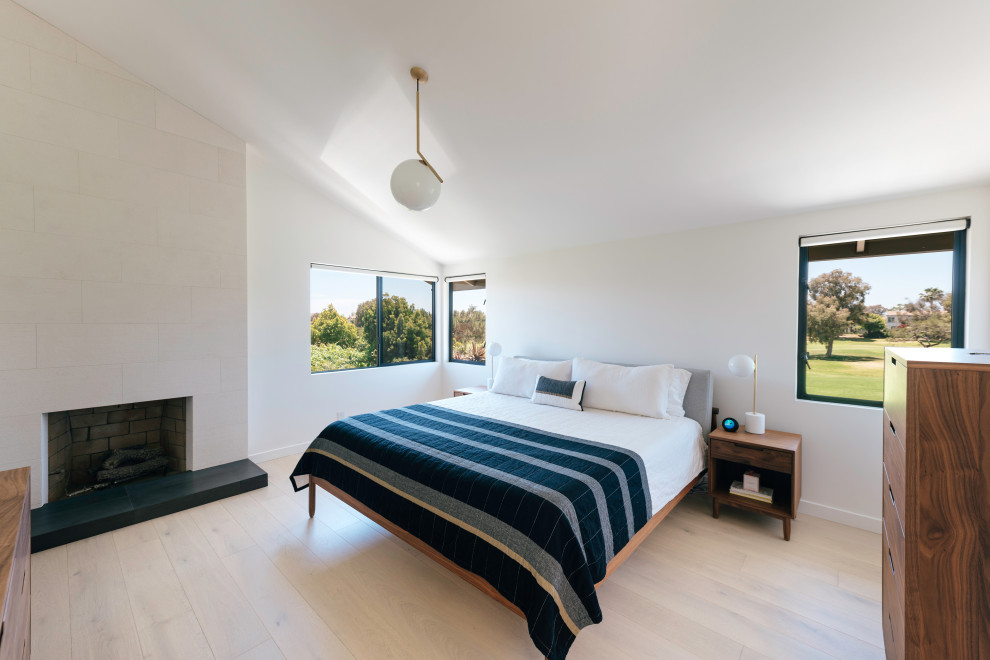 Inspiration for a mid-sized midcentury master bedroom in Orange County with white walls, light hardwood floors, a corner fireplace, beige floor and vaulted.