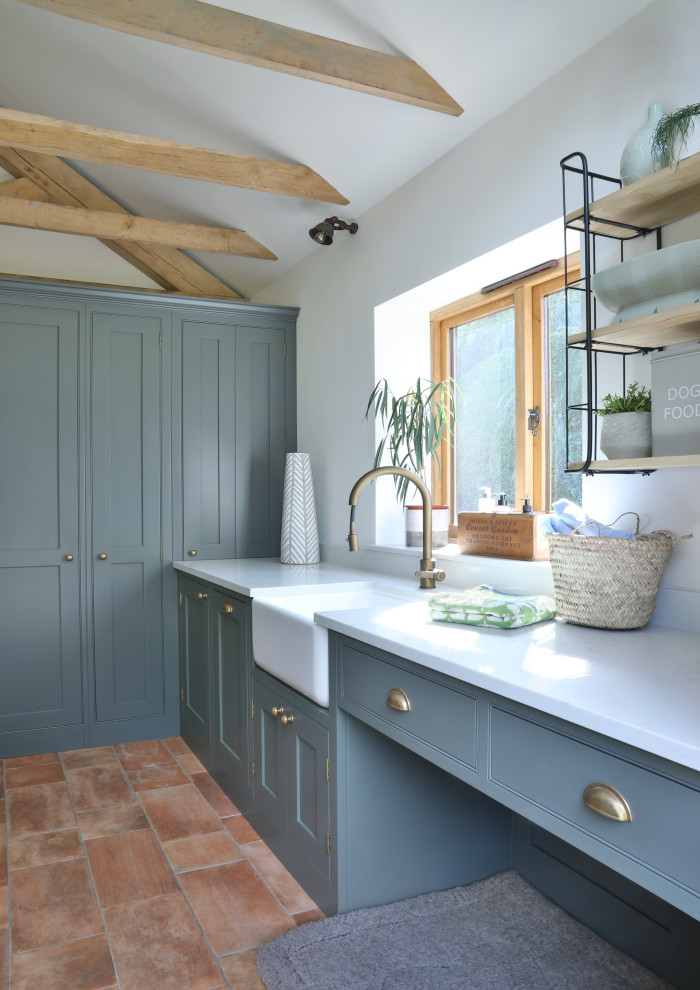 Inspiration for a small traditional l-shaped laundry room in Surrey with a farmhouse sink, shaker cabinets, quartzite benchtops, terra-cotta floors, white benchtop, exposed beam, white walls and a stacked washer and dryer.