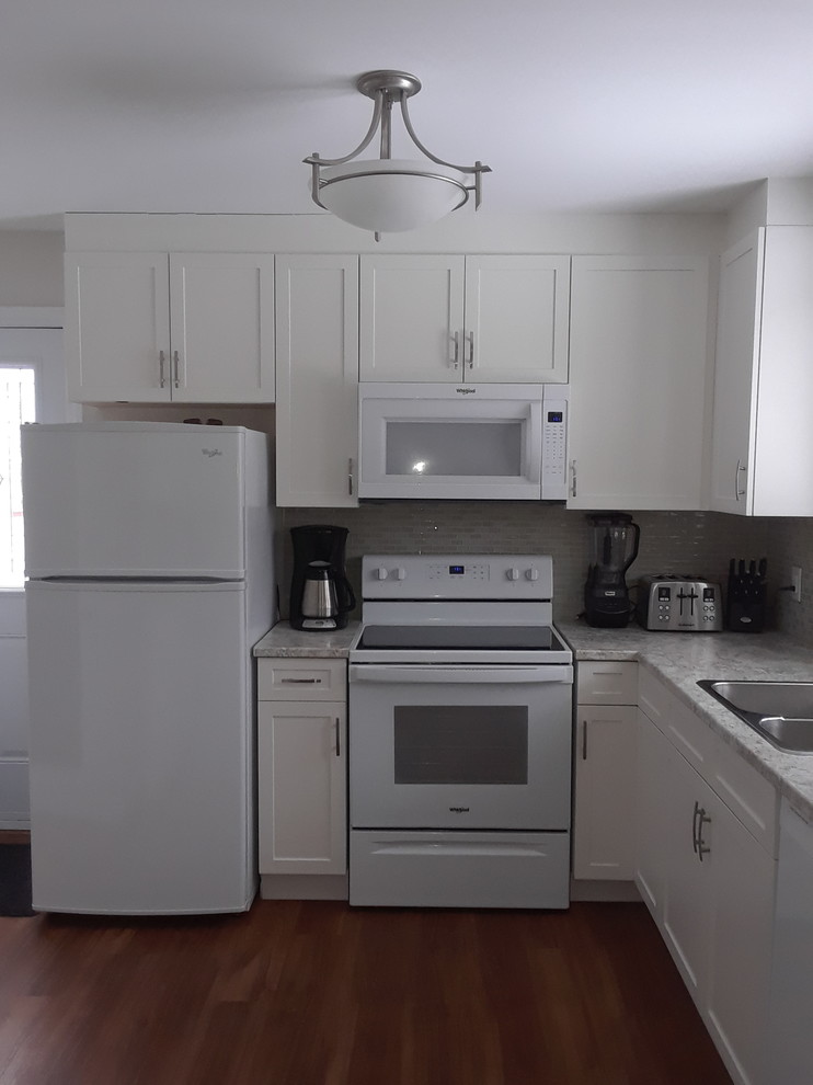 Example of a mid-sized transitional l-shaped enclosed kitchen design with a double-bowl sink, shaker cabinets, white cabinets, laminate countertops, white backsplash, mosaic tile backsplash, white appliances, no island and white countertops