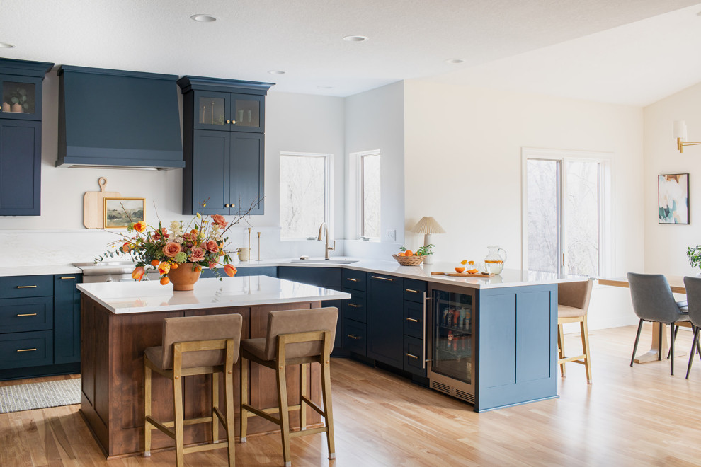 Kitchen - large transitional light wood floor kitchen idea with an undermount sink, shaker cabinets, blue cabinets, quartz countertops, white backsplash, quartz backsplash, stainless steel appliances, an island and white countertops