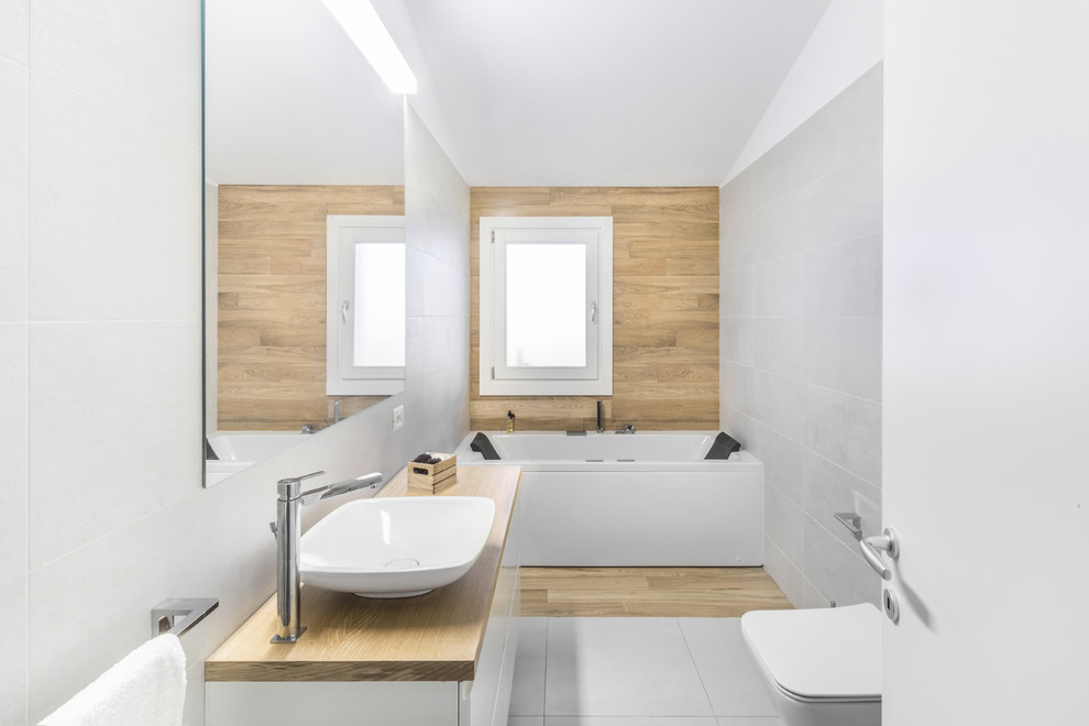 Design ideas for a small contemporary master bathroom in Cagliari with flat-panel cabinets, white cabinets, an alcove tub, a shower/bathtub combo, a wall-mount toilet, gray tile, ceramic tile, a vessel sink, wood benchtops, an open shower, grey walls, grey floor and beige benchtops.