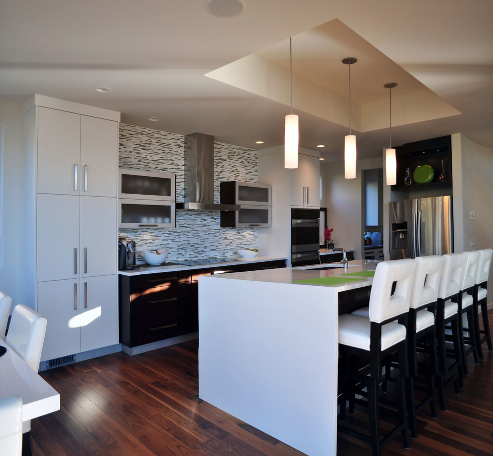 Design ideas for a mid-sized contemporary galley open plan kitchen in Vancouver with an undermount sink, flat-panel cabinets, white cabinets, solid surface benchtops, multi-coloured splashback, glass tile splashback, stainless steel appliances, medium hardwood floors and with island.