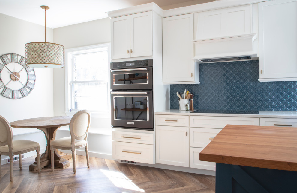 Inspiration for a transitional kitchen in Other with an undermount sink, shaker cabinets, white cabinets, quartz benchtops, blue splashback, ceramic splashback, black appliances, vinyl floors, with island and white benchtop.