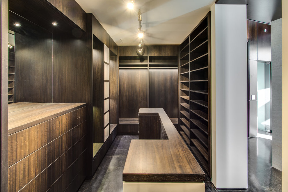Photo of an expansive industrial gender-neutral dressing room in Chicago with open cabinets, dark wood cabinets, concrete floors and black floor.