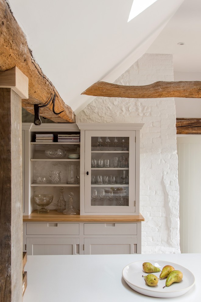 Photo of a large rustic u-shaped kitchen/diner in Other with a belfast sink, shaker cabinets, light wood cabinets, quartz worktops, white splashback, ceramic splashback, stainless steel appliances, ceramic flooring, an island, beige floors, white worktops, exposed beams and feature lighting.