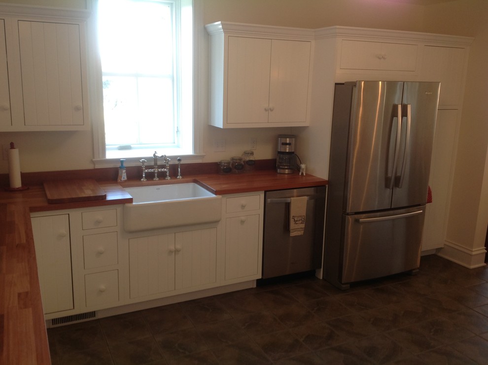 Enclosed kitchen - mid-sized l-shaped medium tone wood floor enclosed kitchen idea with a farmhouse sink, flat-panel cabinets, white cabinets, wood countertops, beige backsplash, stainless steel appliances and no island