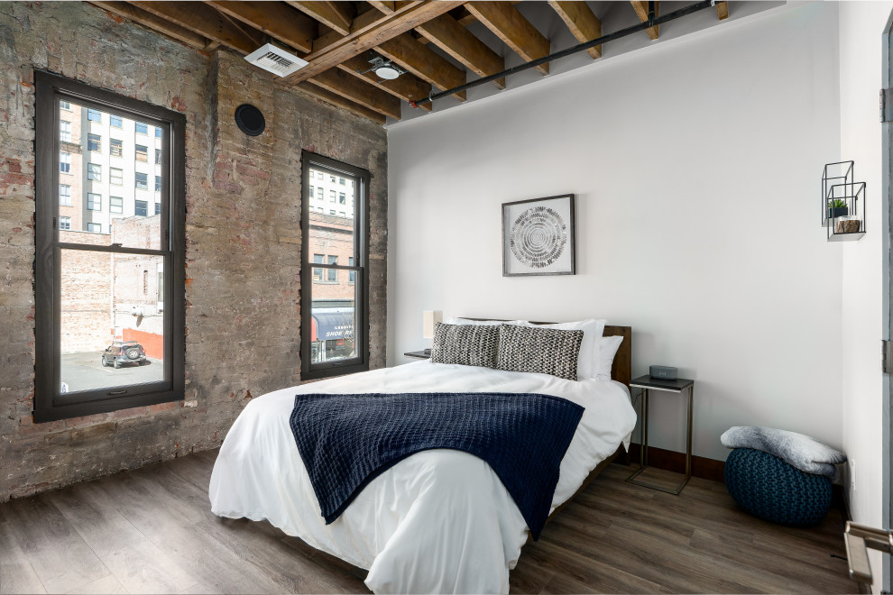 Inspiration for a mid-sized industrial guest bedroom in Other with beige walls, light hardwood floors, no fireplace, brown floor, wood and brick walls.