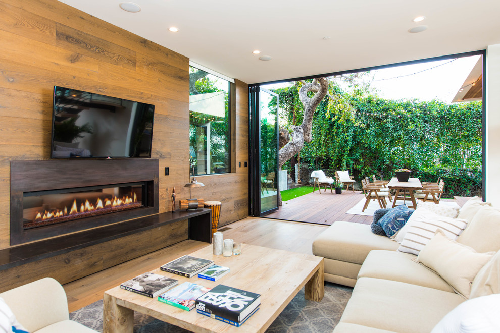 Photo of a beach style family room in Los Angeles with light hardwood floors, a ribbon fireplace, a metal fireplace surround, a wall-mounted tv and beige floor.