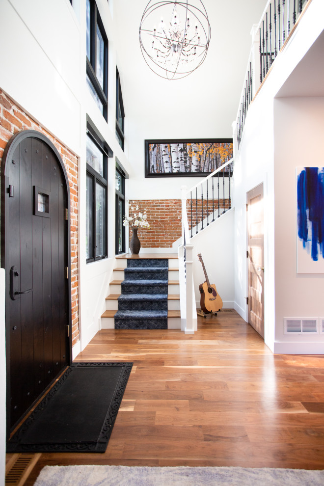 Photo of a transitional foyer in Denver with white walls, medium hardwood floors, a single front door, a black front door, brown floor and brick walls.