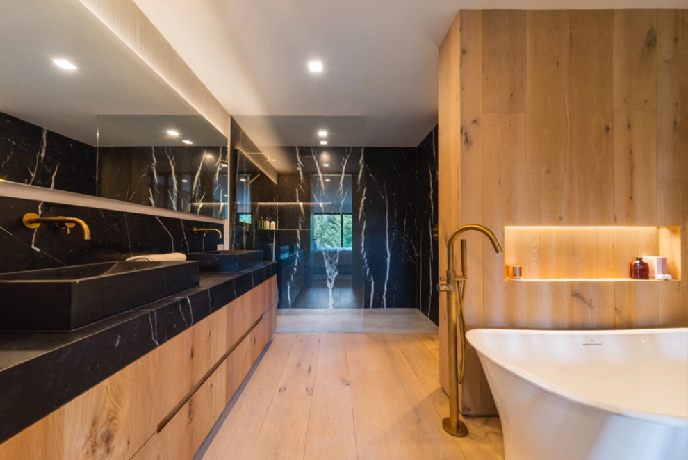 Идея дизайна: ванная комната в современном стиле с отдельно стоящей ванной, душем без бортиков, светлым паркетным полом, открытым душем, черной столешницей, тумбой под две раковины и деревянными стенами