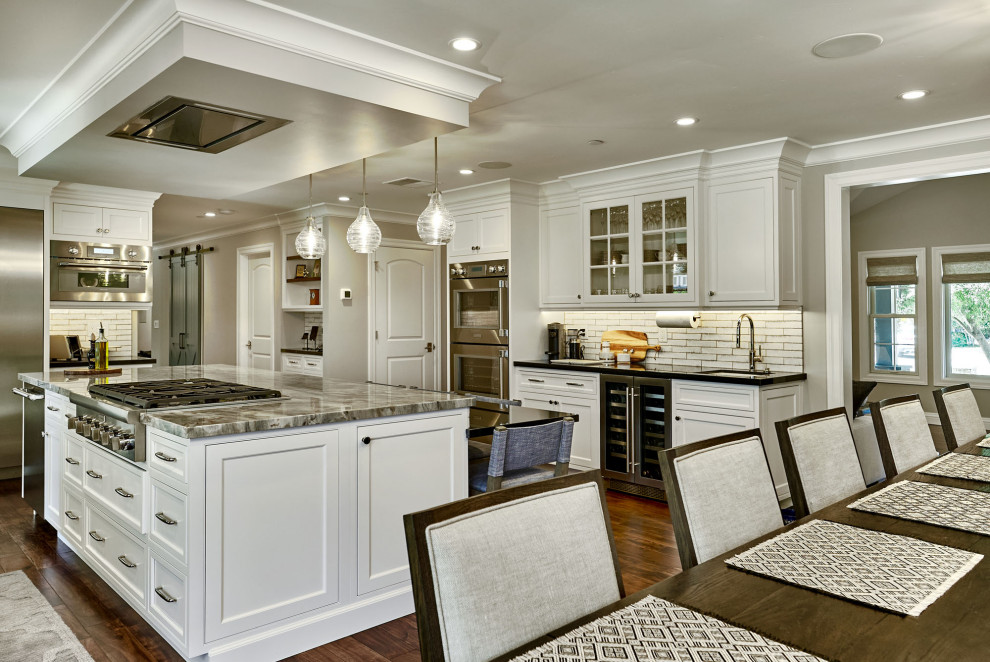 Mid-sized elegant u-shaped medium tone wood floor and brown floor eat-in kitchen photo in San Francisco with an undermount sink, shaker cabinets, white cabinets, gray backsplash, subway tile backsplash, stainless steel appliances, an island and multicolored countertops