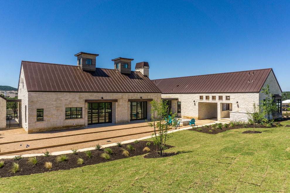 Photo of a large country one-storey white house exterior in Austin with stone veneer, a shed roof and a metal roof.