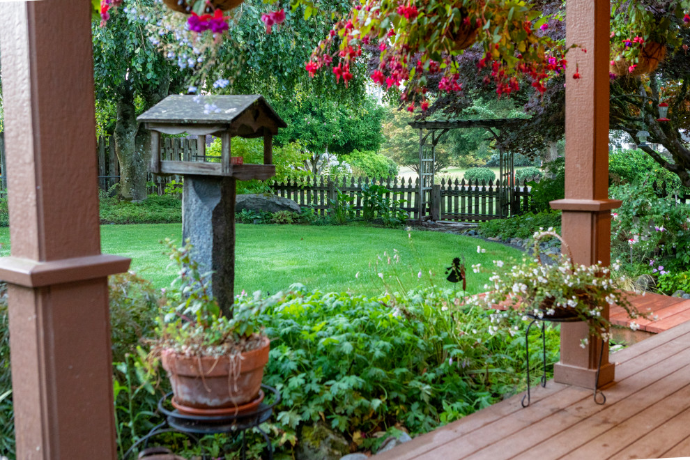 На фото: большой участок и сад на заднем дворе в викторианском стиле с покрытием из каменной брусчатки и с деревянным забором