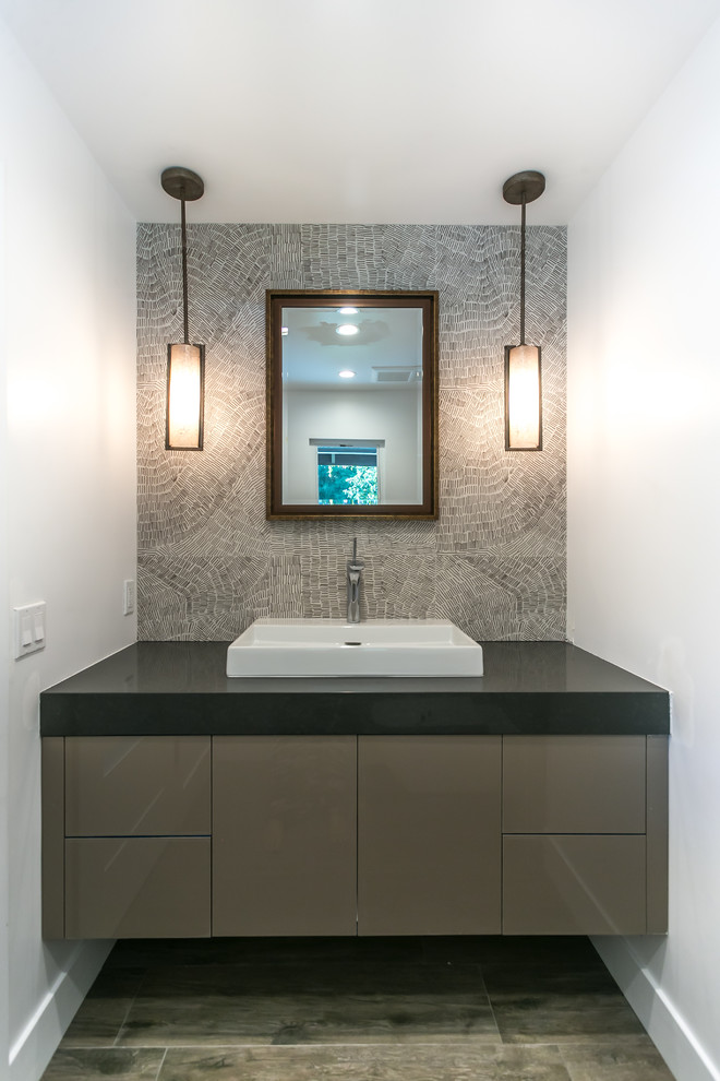 Design ideas for a mid-sized modern powder room in Los Angeles with a drop-in sink, brown cabinets, engineered quartz benchtops, white walls, ceramic floors, gray tile and black benchtops.