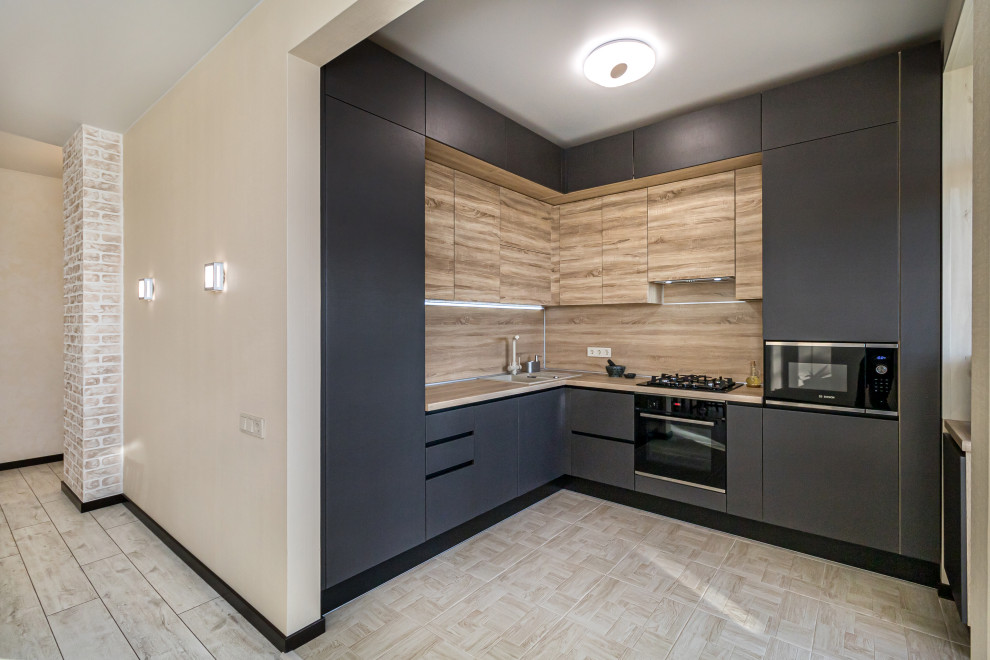 Photo of a mid-sized contemporary l-shaped open plan kitchen in Other with a drop-in sink, flat-panel cabinets, grey cabinets, laminate benchtops, black appliances, porcelain floors, no island and beige floor.