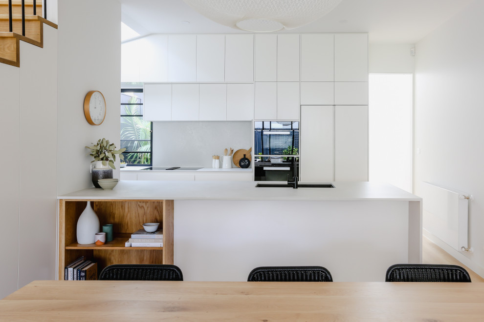 This is an example of a contemporary galley kitchen in Melbourne with an undermount sink, flat-panel cabinets, white cabinets, white splashback, stainless steel appliances, medium hardwood floors, a peninsula, brown floor and white benchtop.