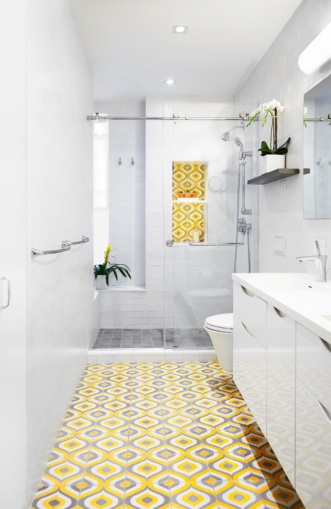 Inspiration for a contemporary 3/4 bathroom in New York with flat-panel cabinets, white cabinets, a wall-mount toilet, yellow tile, gray tile, multi-coloured tile, white tile, cement tile, white walls, cement tiles, solid surface benchtops, an alcove shower and a sliding shower screen.
