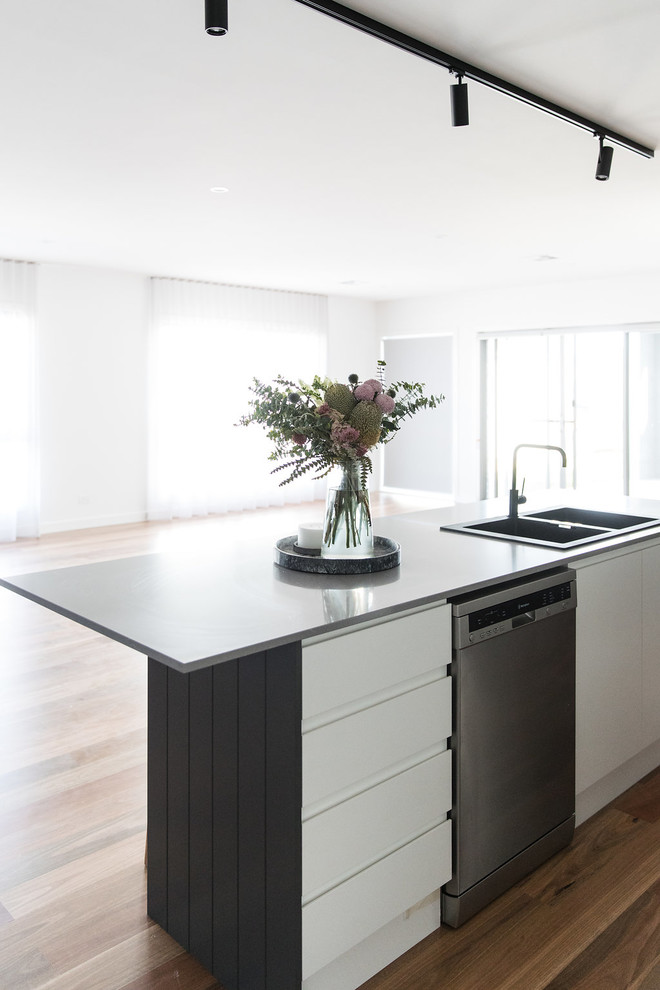 This is an example of a mid-sized modern galley open plan kitchen in Canberra - Queanbeyan with a double-bowl sink, black cabinets, quartz benchtops, grey splashback, subway tile splashback, black appliances, medium hardwood floors, with island and brown floor.